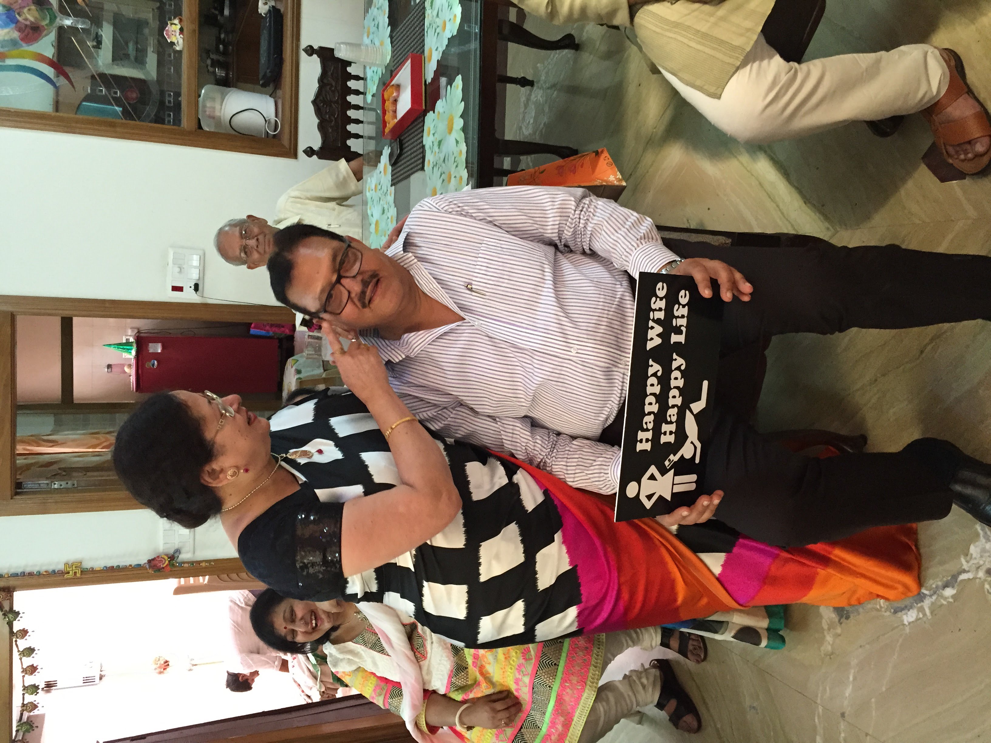 Beena Mehrotra and Mukesh Mehrotra at a family celebration in Kashipur — Mummy holding Papa's face while he holds a 'Happy Wife Happy Life' sign, the affection and humour of a long marriage on full display